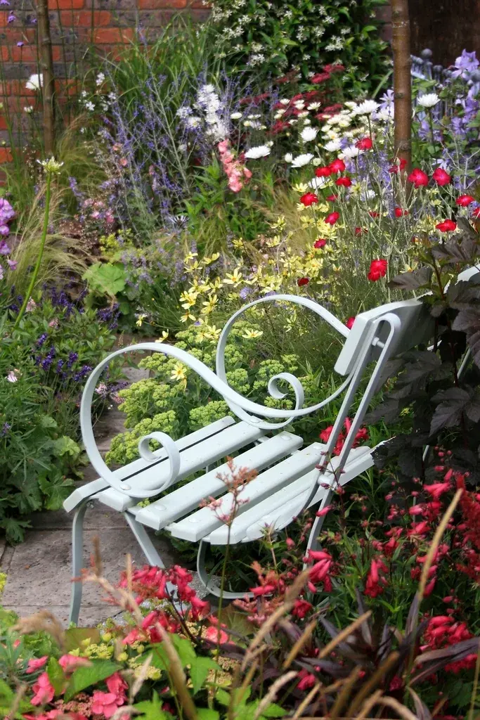 Eine helle Gartenbank zwischen roten und lila Blumen